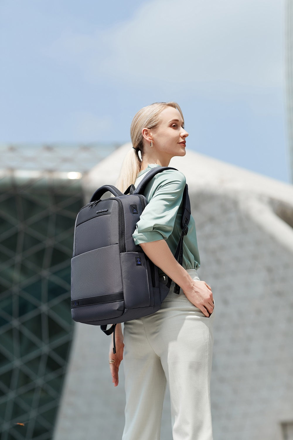 Frau im Business-Outfit trägt einen modernen Business-Rucksack in einer urbanen Stadtkulisse.