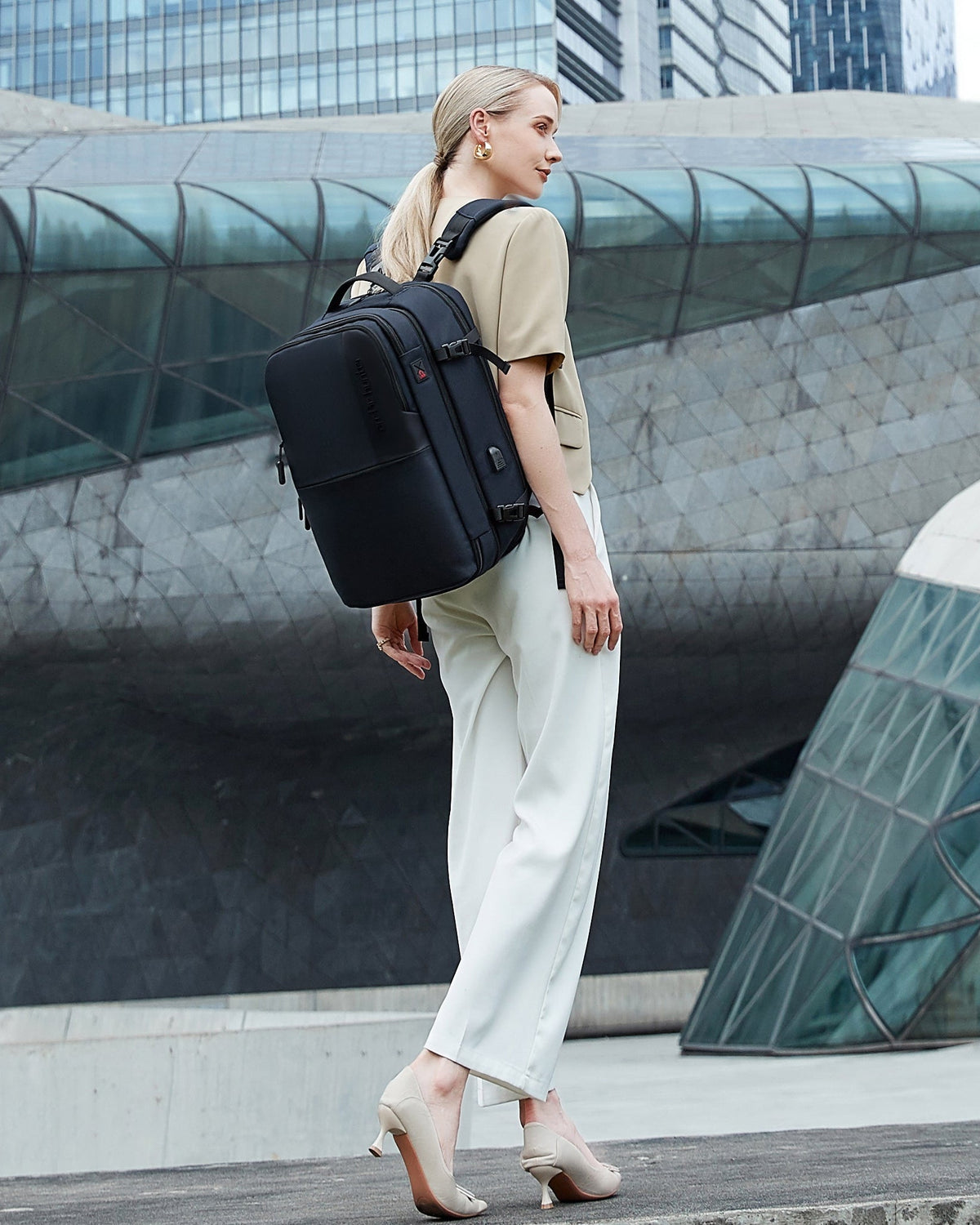 Eine Frau im Business-Outfit mit Business-Laptop-Rucksack unterwegs in einer urbanen Stadtkulisse