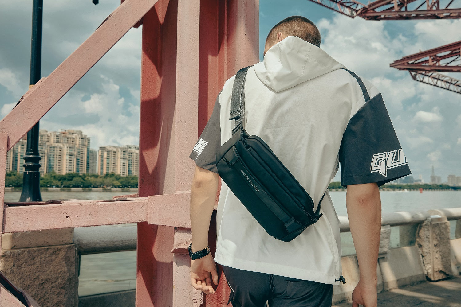Moderner Mann trägt die schwarze Arctic Prox Crossbody Tasche im urbanen Outdoor-Look auf einer Brücke – ideal für Stadtentdecker.