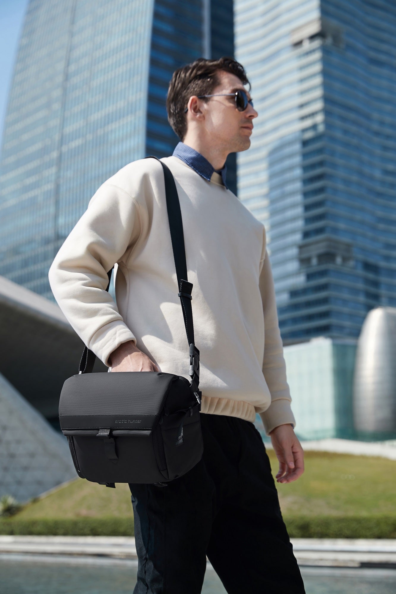 Fotograf hält die ArcticFlex Pro Kameratasche in der Hand, mit moderner Architektur im Hintergrund – steht für Qualität und Abenteuerlust.