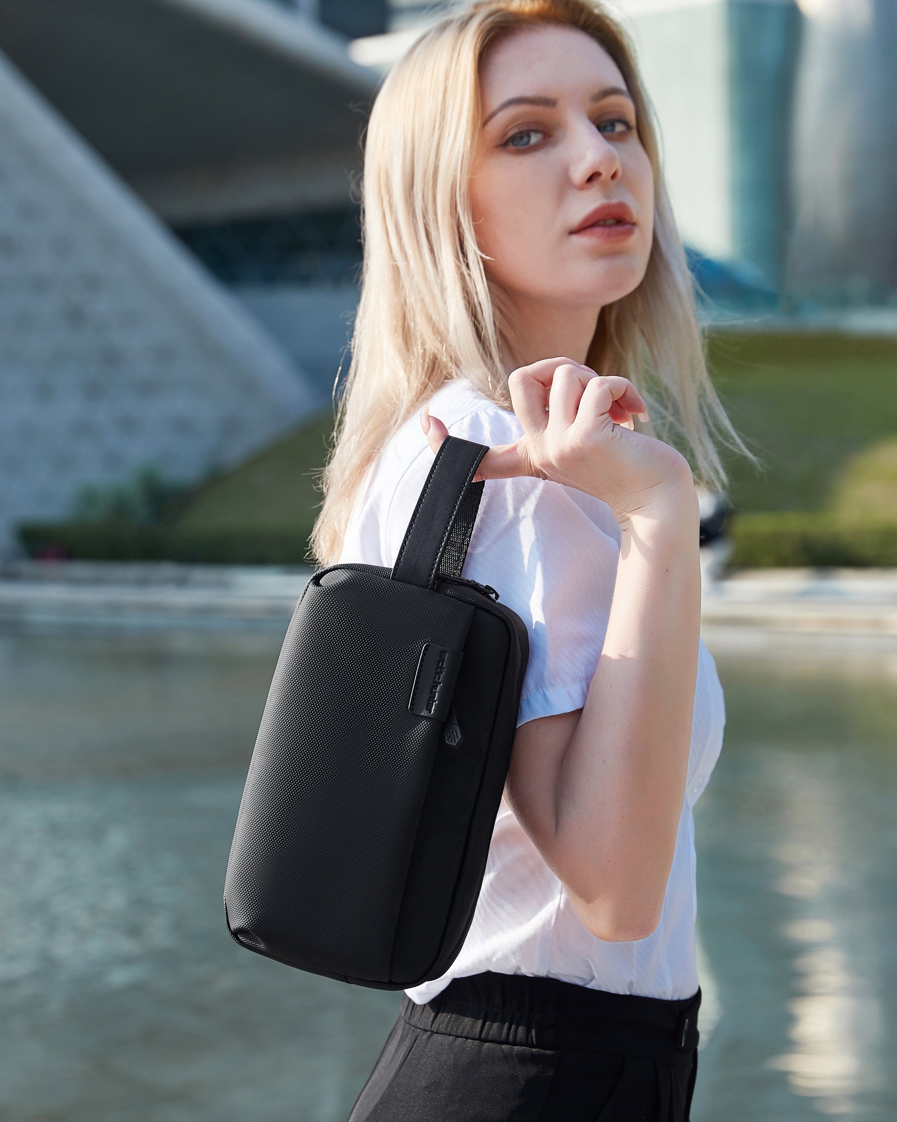 Frau trägt schwarze Travel Pouch Lite Crossbody – unisex, wasserabweisende Tasche für Alltag, Reisen und Arbeit