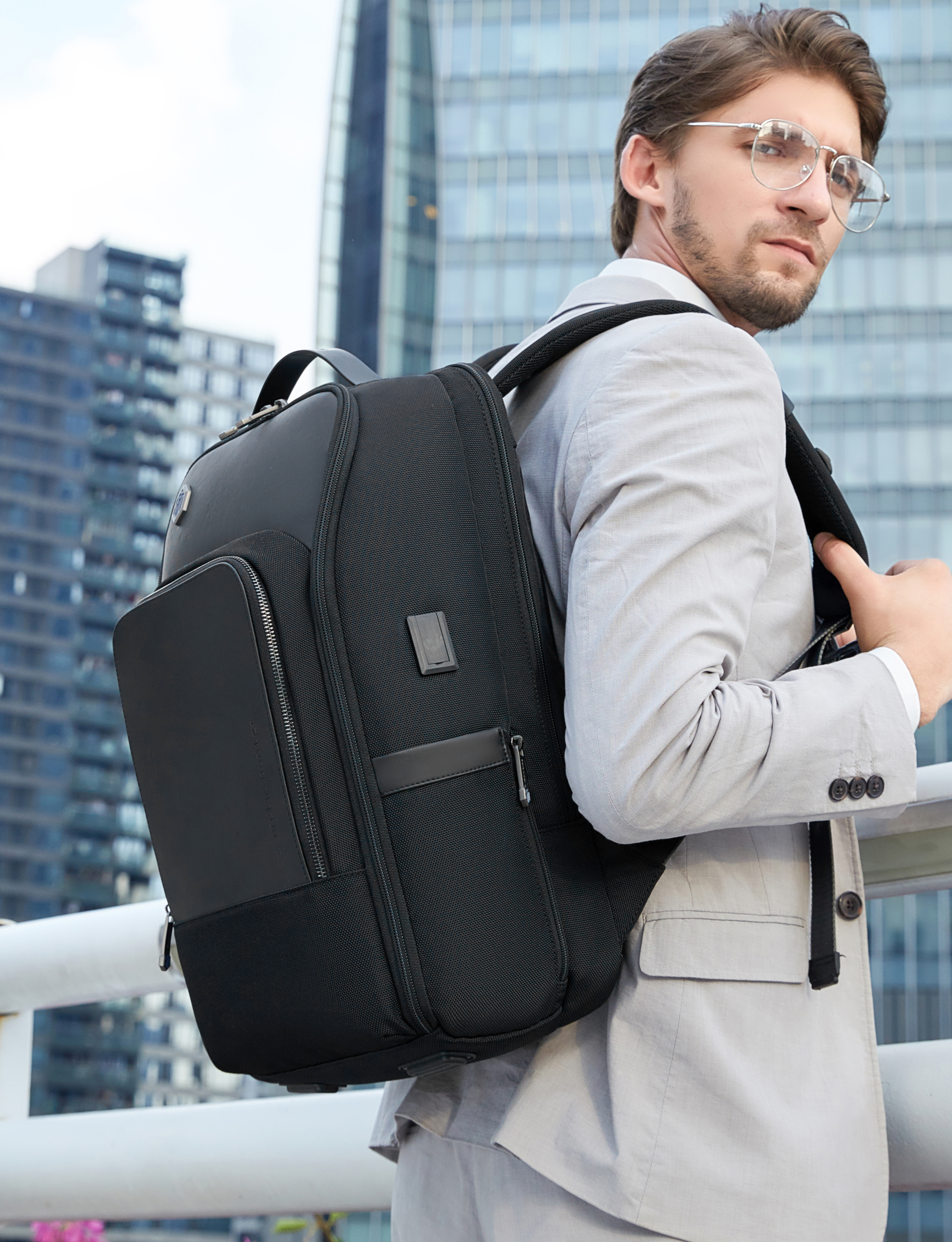 Mann im Business-Outfit trägt einen schwarzen Business-Rucksack vor moderner Stadtkulisse.