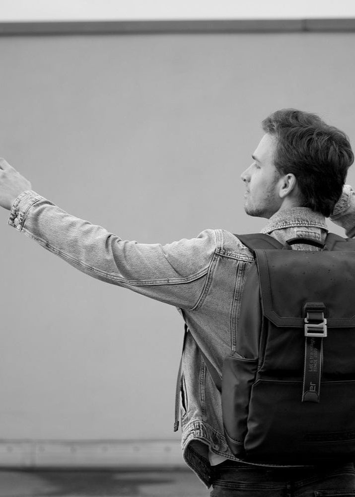 Mann trägt einen modernen schwarzen Herren-Rucksack in urbaner Umgebung – ideal als Weihnachtsgeschenk 2025.