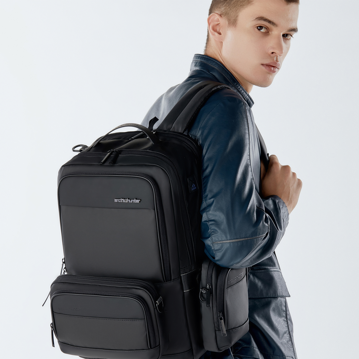 Mann trägt einen schwarzen, modernen Herren-Rucksack mit mehreren Fächern und organisiertem Design.