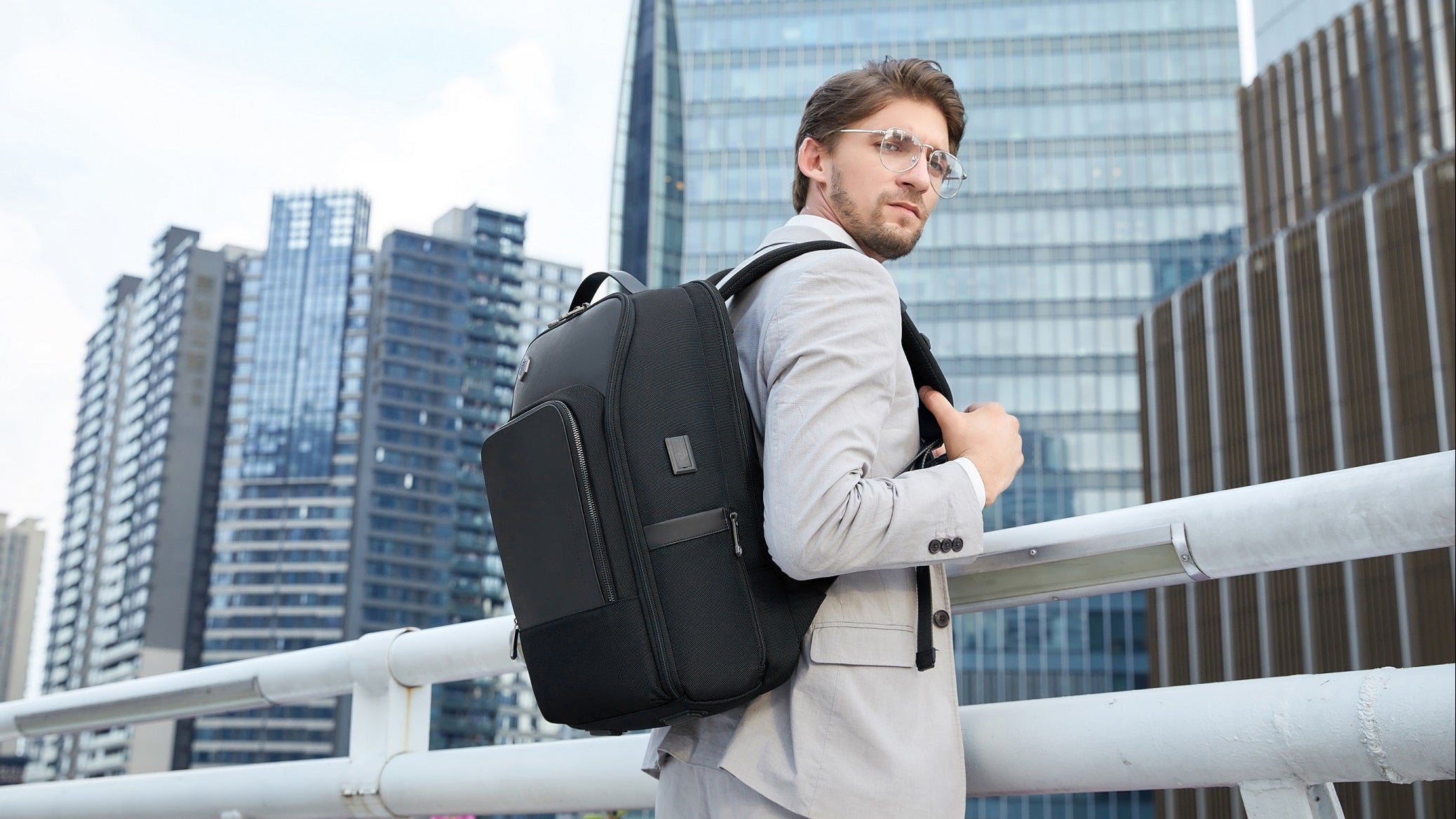 Mann im Business-Outfit trägt einen schwarzen Business-Rucksack vor moderner Stadtkulisse.