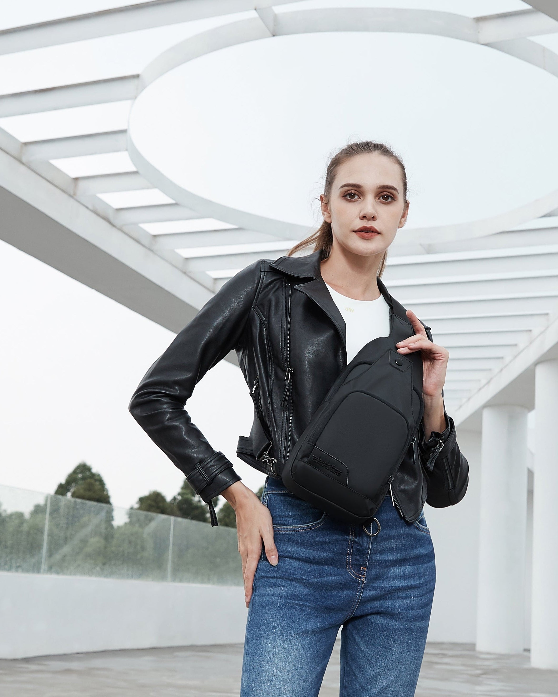 Frau trägt eine moderne schwarze Crossbody-Bag vor futuristischer Architektur in einer urbanen Umgebung.