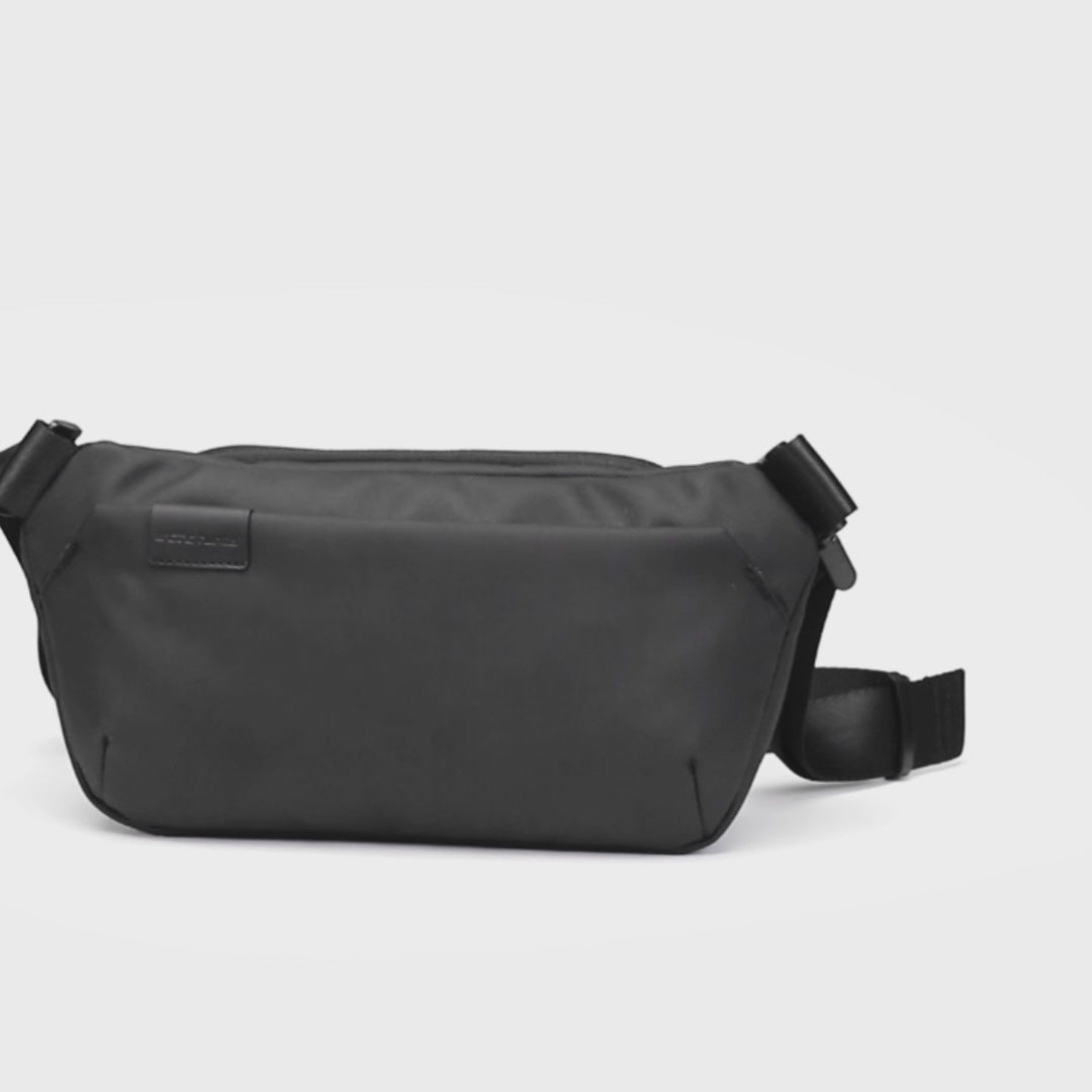Video zeigt, wie Smartphone, Geldbörse, Tablet und weitere Essentials in der Chill Crossbody Tasche verstaut werden. Anschließend tragen ein Mann und eine Frau die Tasche im Alltag vor urbaner Stadtkulisse.