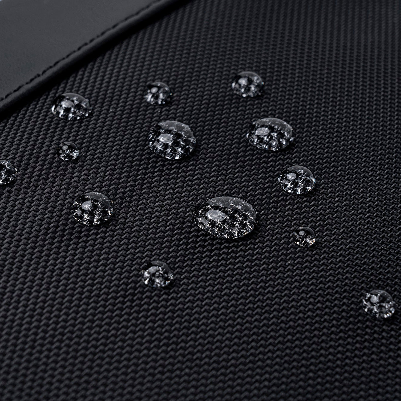 Detailaufnahme eines SC-Bag Rucksacks, auf dessen wasserabweisender Oberfläche Wassertropfen sichtbar abperlen, ideal für Schutz bei Regen