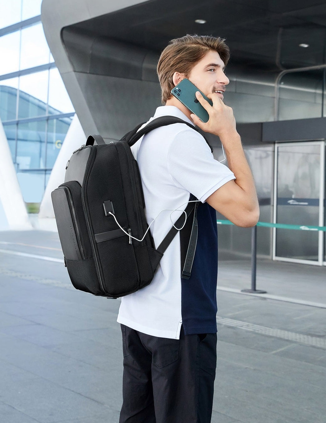 Mann telefoniert unterwegs mit angeschlossenem Smartphone, getragenem Travel Chic Rucksack mit integriertem USB-Anschluss.